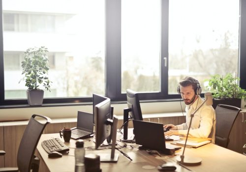 Servicemitarbeiter in weißem Hemd mit Headset am PC und Laptop im Büro