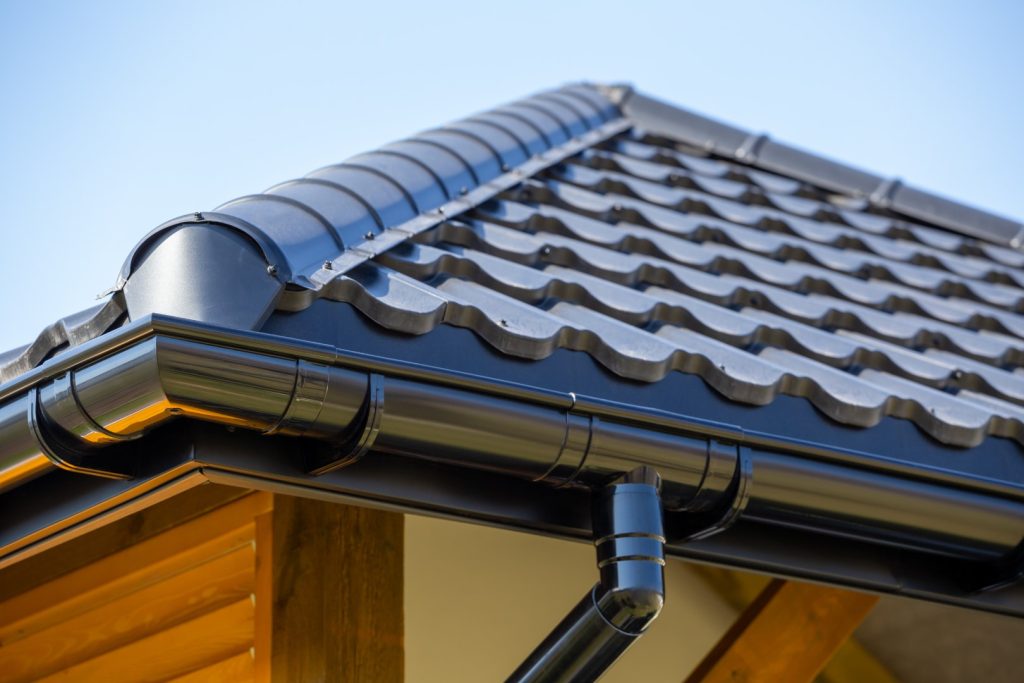 Seitenansicht eines perfekt verarbeiteten Dachs mit Holzfassade und Dachrinne unter blauem Himmel