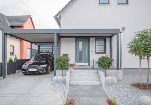 Neues Einfamilienhaus in hellgrau Frontansicht mit Eingangsbereicht, schwarzem PKW in der Garage und Steingarten