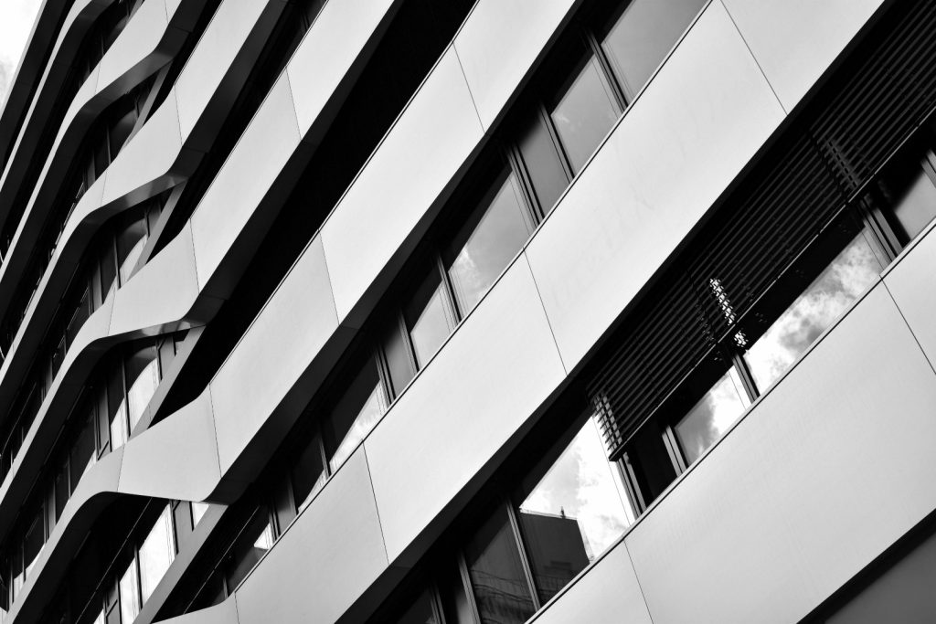 Schwarz/weiss Foto einer modernen und sauberen Fassade, im Fenster spiegeln sich Wolken